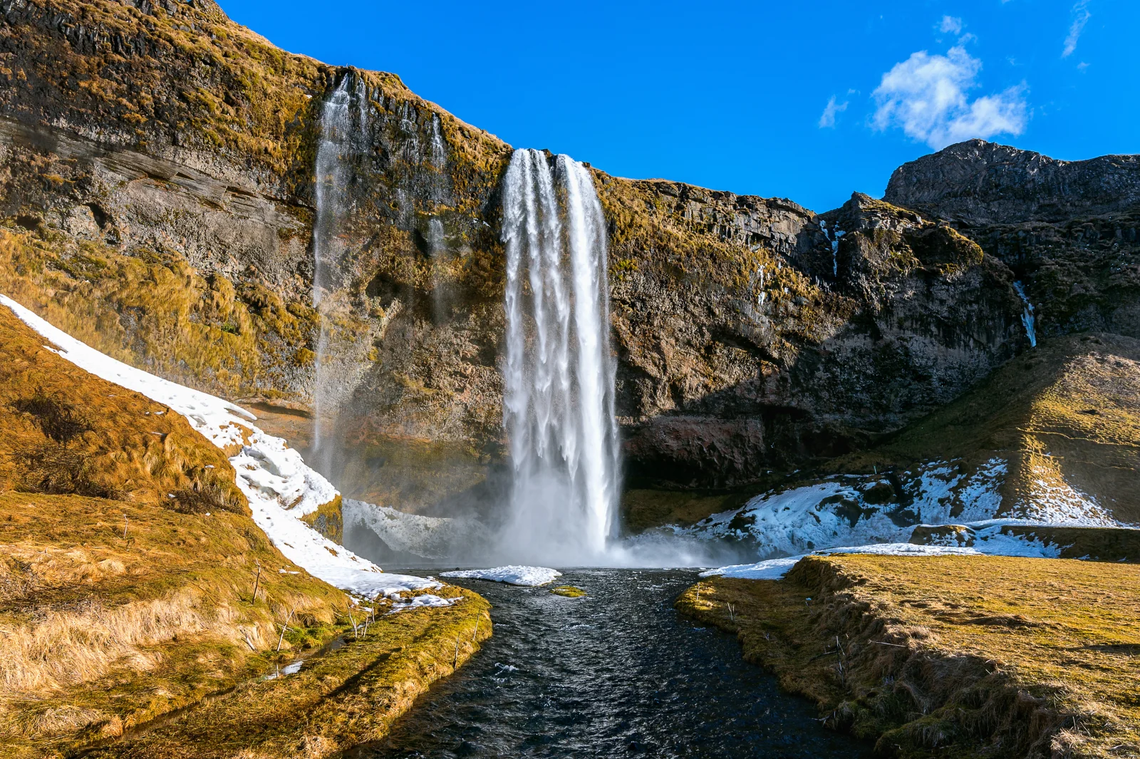 Waterfall cascading over rocky cliffs into a stream surrounded by patches of snow
