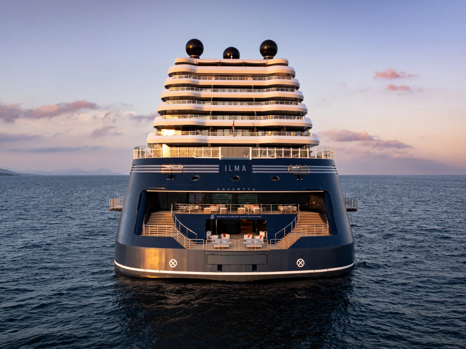 Stern view of Ilma with illuminated decks beneath a pastel evening sky
