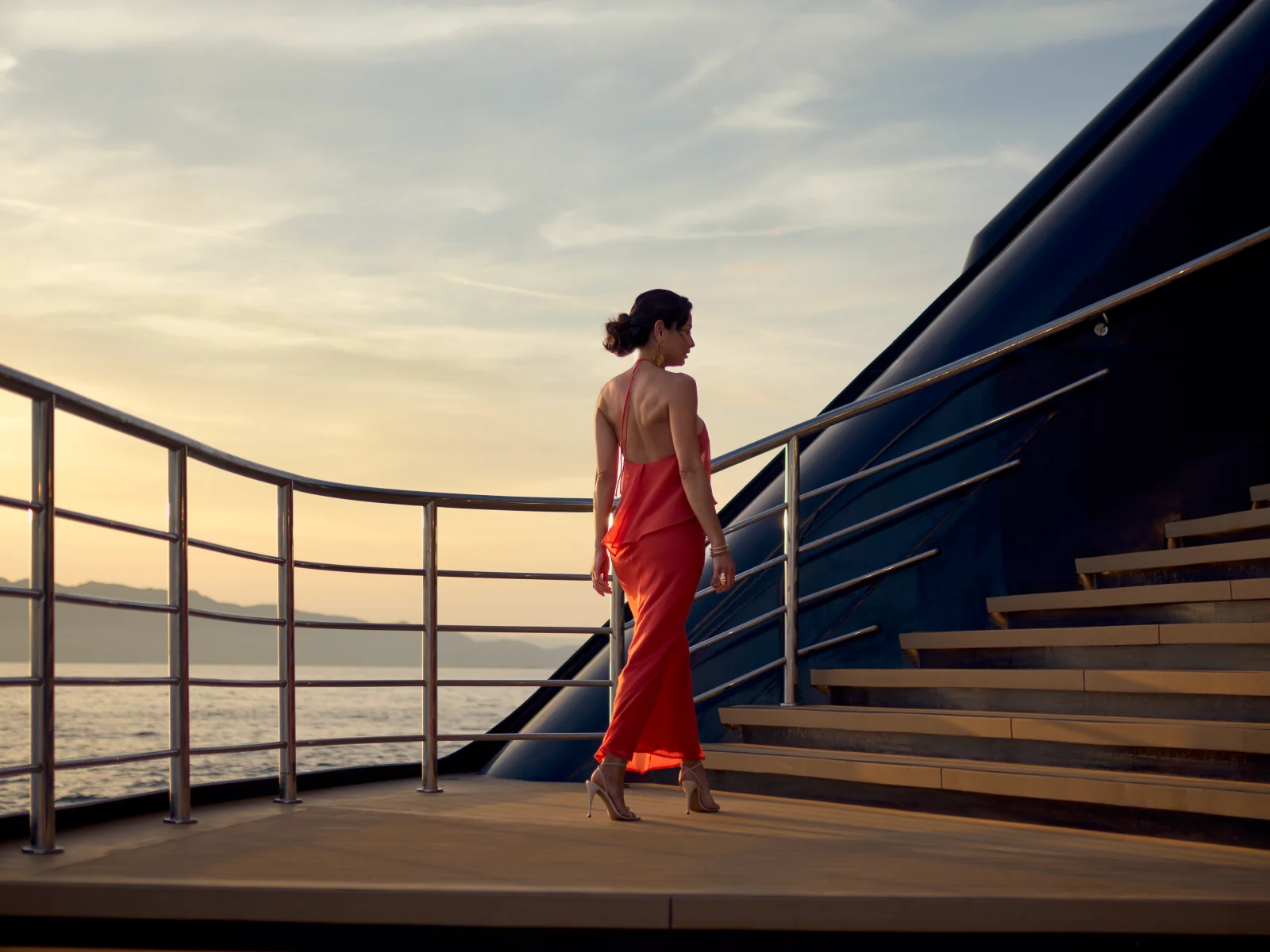 A guest in a red dress ascending the marina steps aboard Luminara at sunset